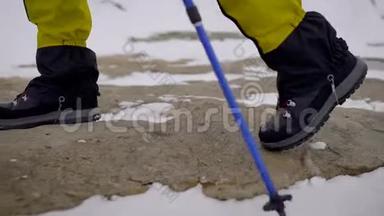 一个徒步旅行者穿着沉重的靴子`腿的特写镜头和徒步旅行者在雪地和岩石上行走的徒步旅行者。